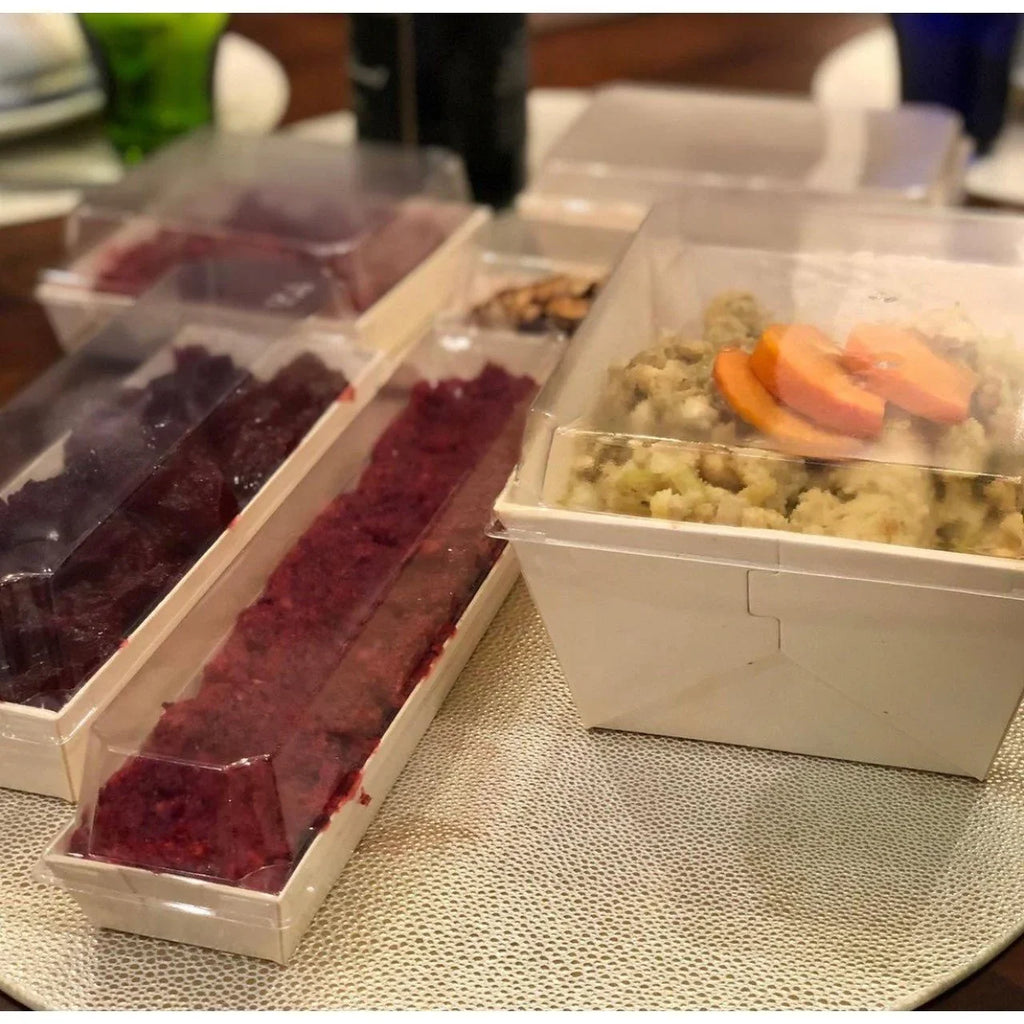 Assorted food items in containers with clear lids on a textured surface