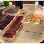Assorted food items in containers with clear lids on a textured surface