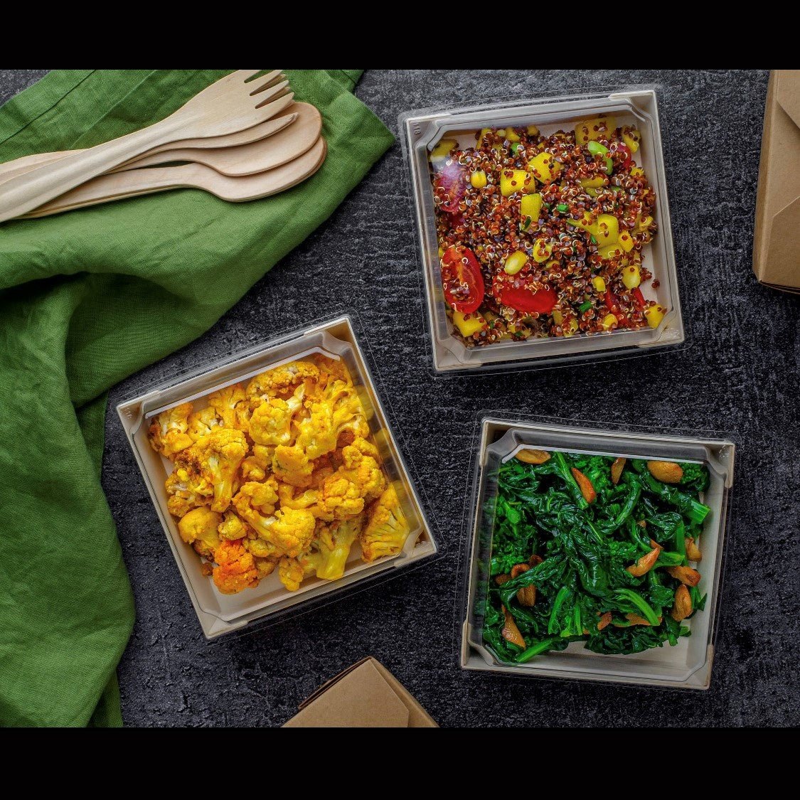 Three containers of different vegetable dishes on a dark surface with a green cloth and wooden utensils.