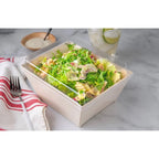 Salad in a take-out container with lid on a marble surface with a fork and towel.