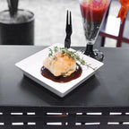 White dessert plate with a dessert pastry over a dark sauce, garnished with herbs, on a black table.