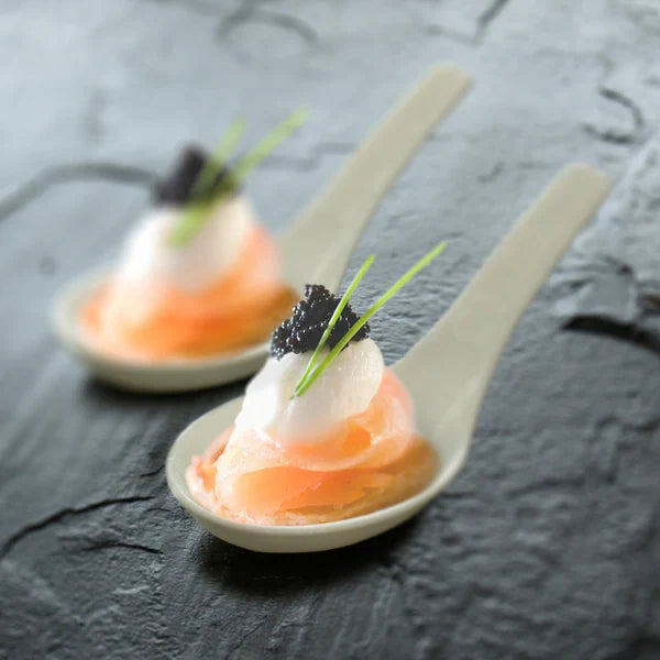 Two small asian spoons with appetizers on a dark textured surface