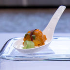 White appetizer spoon with a small portion of food on a reflective surface