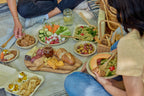 Charcuterie served using compostable bowls, plates, and clamshells on a picnic blanket.