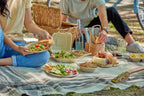 Compostable tableware including plates, clamshells, and bowls being used at an outdoor picnic.