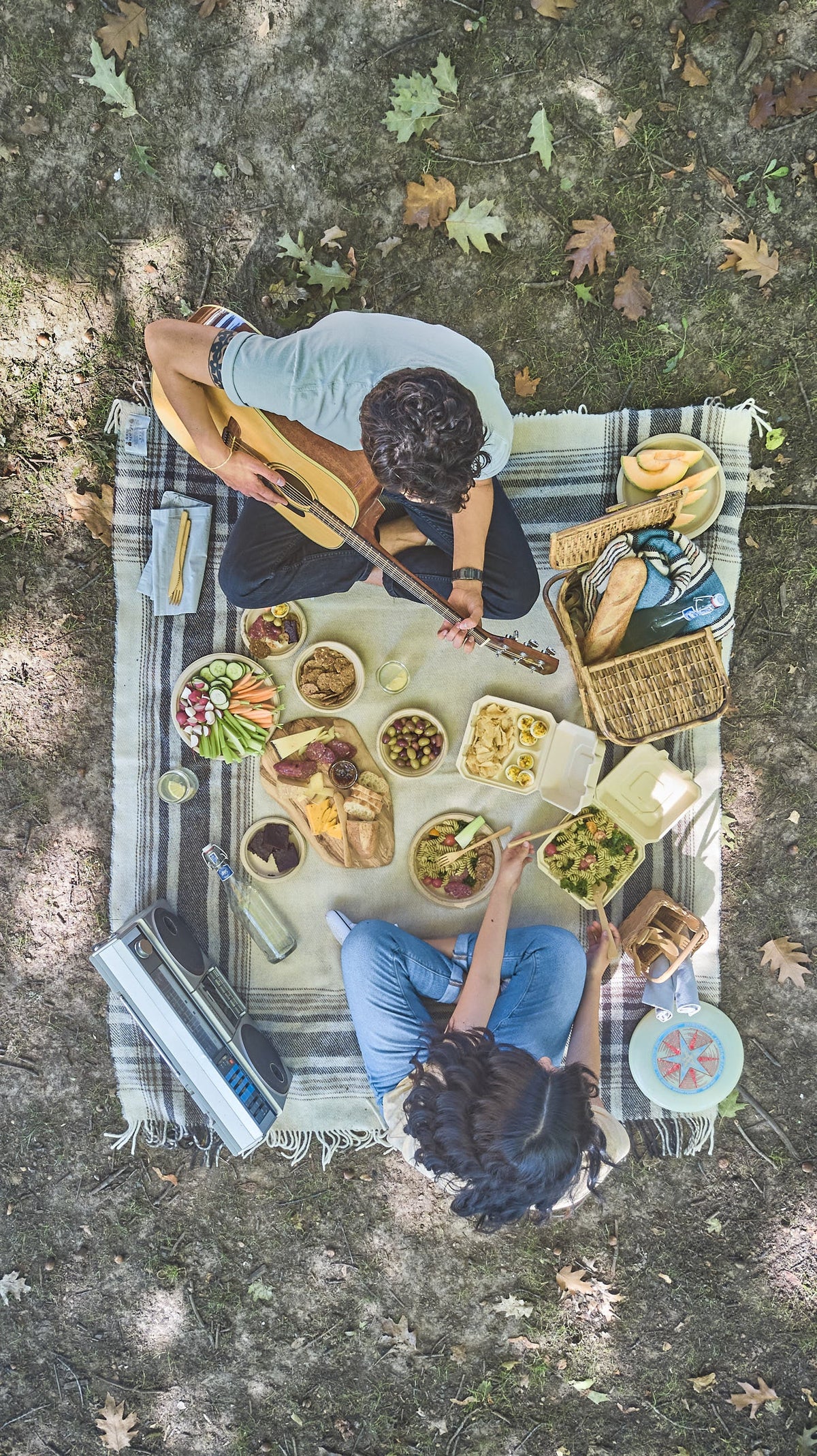 Two people having a picnic in the park, using compostable plates, bowls, and clamshells for their meal.