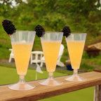 Three glasses of orange juice with blackberries on a wooden ledge outdoors.